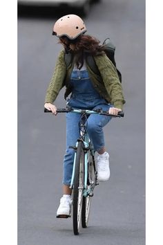 a woman riding a bike down a street with a helmet on her head and wearing overalls