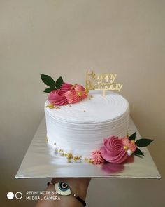 a white cake with pink and yellow flowers on top is being held by a woman's hand