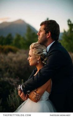 a bride and groom embracing each other on their wedding day in front of the mountains