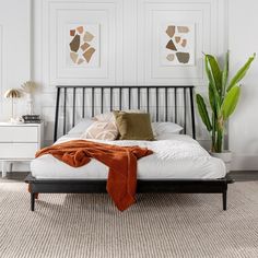 a bed with white sheets and pillows in a bedroom next to a potted plant