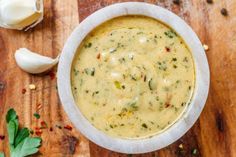 a bowl filled with soup sitting on top of a wooden table next to garlic and parsley