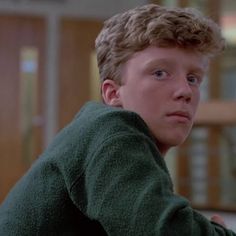 a young man with curly hair wearing a green sweater looking at the camera while sitting down