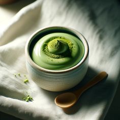 a bowl filled with green liquid next to a spoon on top of a white cloth