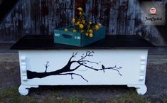 a painted chest with a tree on it and flowers in the top drawer, sitting next to a wooden fence