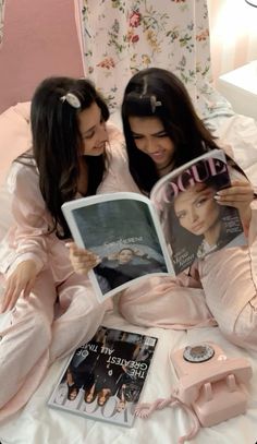 two girls in pink pajamas reading magazines on a bed