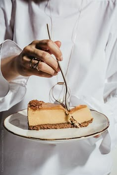 a woman is holding a plate with a piece of cake on it and a fork in her hand