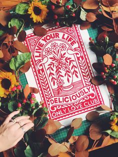 someone is holding up a red and white piece of paper with flowers on it, surrounded by sunflowers