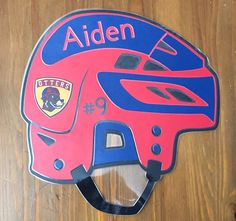 a pink helmet with blue accents is on a wooden surface and has the name alden written on it