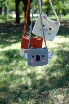 two crocheted purses hanging from a string in the grass with trees in the background