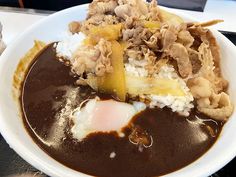 a white bowl filled with rice and meat covered in sauce on top of a table