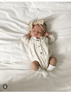 a baby is sleeping on a white bed with a bow in it's hair