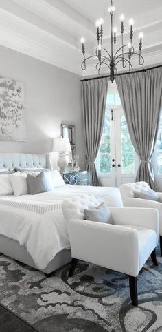 a large white bed sitting in a bedroom next to two chairs and a chandelier