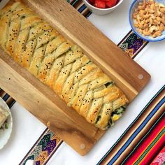 a wooden cutting board topped with bread next to bowls of fruit and nuts