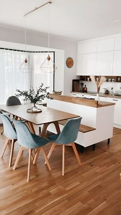 a kitchen with wooden floors and white cabinetry has a dining table surrounded by blue chairs