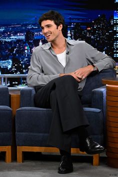 a man sitting on top of a blue couch in front of a tv screen and smiling