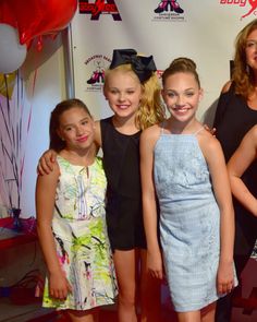 a group of girls standing next to each other in front of a red carpeted wall