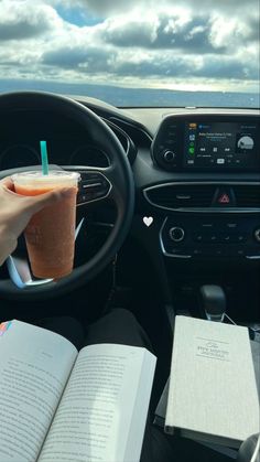 a person holding a drink in their hand while driving with an open book on the steering wheel