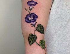 a woman's arm with purple flowers and green leaves on the left side of her arm