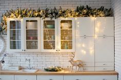 a kitchen with white cabinets and christmas lights on the windowsills, along with deer figurines