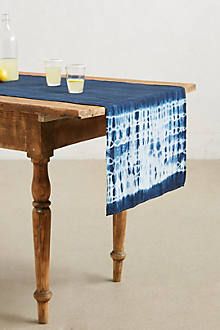 a wooden table topped with a blue tie - dyed table runner next to a bottle of lemonade