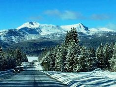 the road is lined with snow covered trees and mountains in the distance are all around