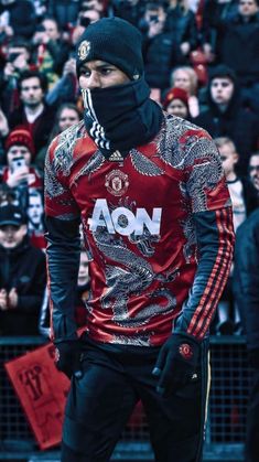 a man in a red shirt and black hat is wearing a face mask as he stands in front of a crowd