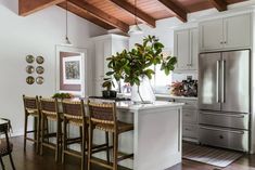 a kitchen with white cabinets and wooden floors, an island in front of the refrigerator