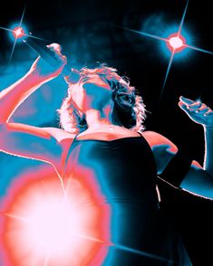 a woman singing into a microphone in front of red and blue lights with her hands up