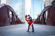 a man and woman kissing on a bridge in the middle of a city with tall buildings behind them