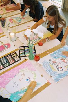 several children are sitting at a table with their artwork on it and one child is drawing