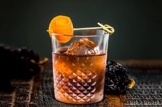 a glass filled with liquid and an orange peel on top of a table next to blackberries