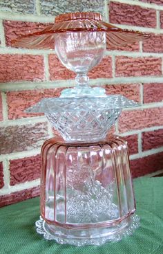 a glass candle holder sitting on top of a green tableclothed cloth next to a brick wall