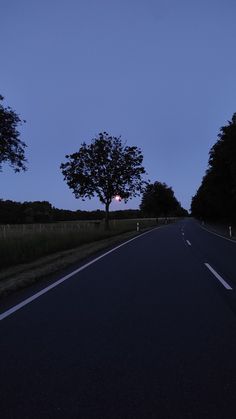 an empty road at dusk with trees on both sides and the sun in the distance