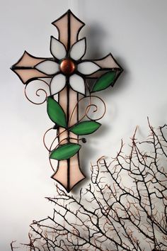 a stained glass cross hanging from the side of a wall next to a twig