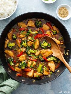 chicken and broccoli stir frying in a skillet with wooden spoons