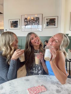 three women sitting at a table drinking coffee and talking to each other with their mouths open