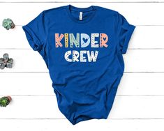 a blue shirt that says kinder crew on it next to succulents