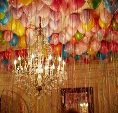 a chandelier hanging from the ceiling with many balloons in the air behind it