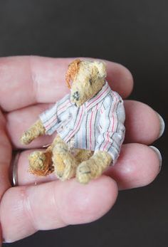 a small teddy bear in a shirt is held in someone's hand