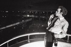 a man standing on top of a balcony next to a crowd at night holding a beer