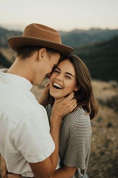 a man and woman are standing together in the mountains, smiling at each other with their faces close to one another