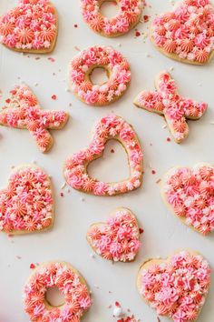 decorated cookies arranged in the shape of hearts and flowers on a white surface with pink sprinkles