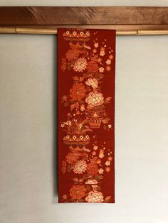 a red wall hanging with flowers and leaves on it's side in front of a white wall