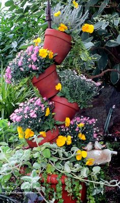 several red flower pots are stacked on top of each other in a garden filled with flowers