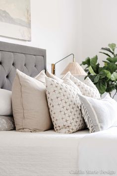 a bed topped with lots of pillows next to a plant