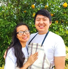 a man and woman standing next to each other in front of trees with oranges