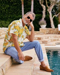 an older man sitting on the edge of a pool with his feet propped up to his face