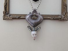 a white mask hanging from a silver frame on a wall next to a framed photograph