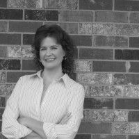 a black and white photo of a woman standing in front of a brick wall with her arms crossed