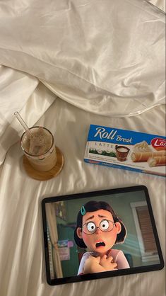 a tablet with an animated face sitting on a bed next to a box of cereal